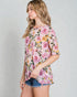 Woman wearing a floral print top and denim shorts on a plain background