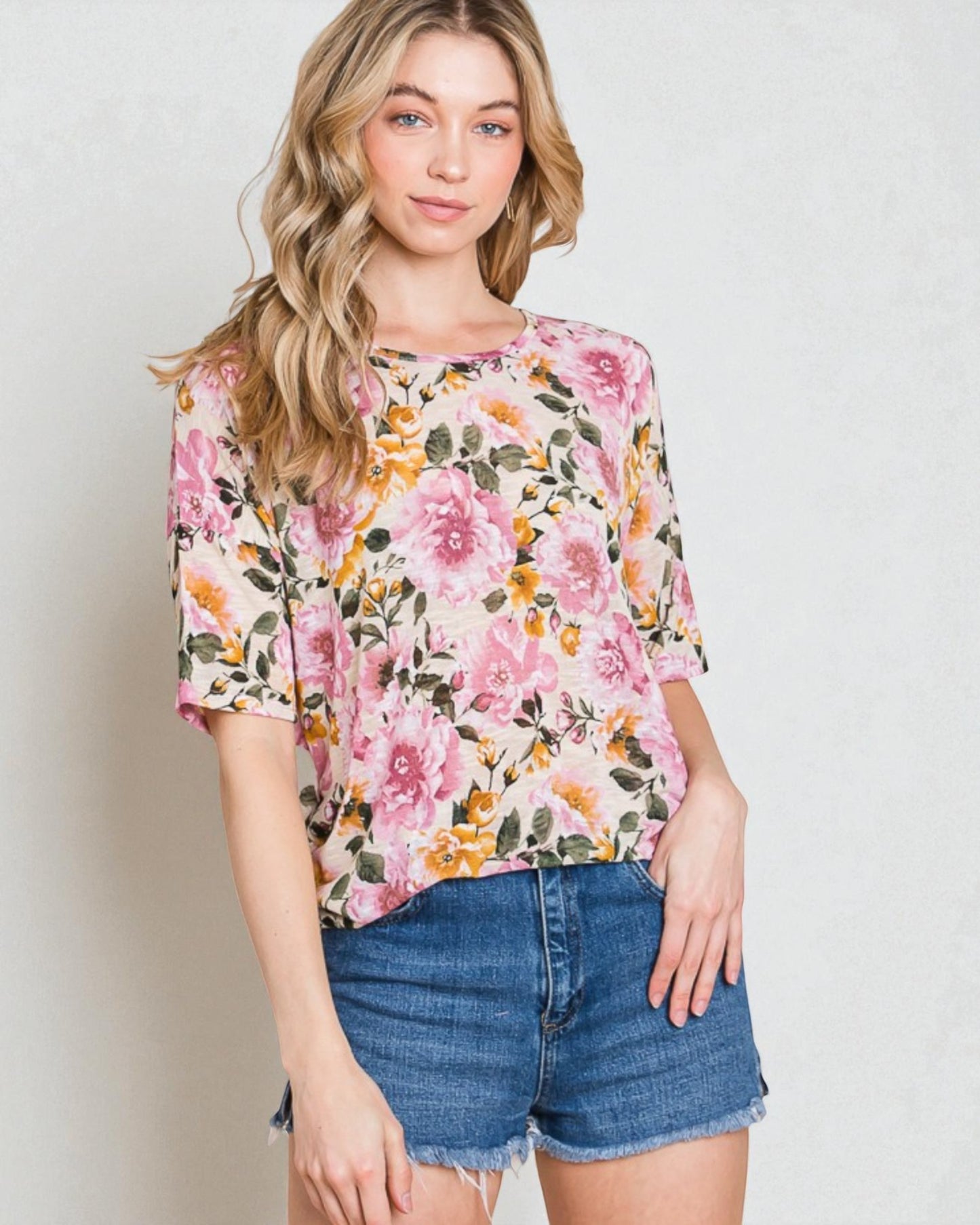 Woman wearing a floral blouse and denim shorts against a plain background