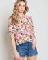Woman wearing a floral blouse and denim shorts against a plain background