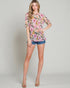 Woman wearing a floral blouse and denim shorts on a plain background