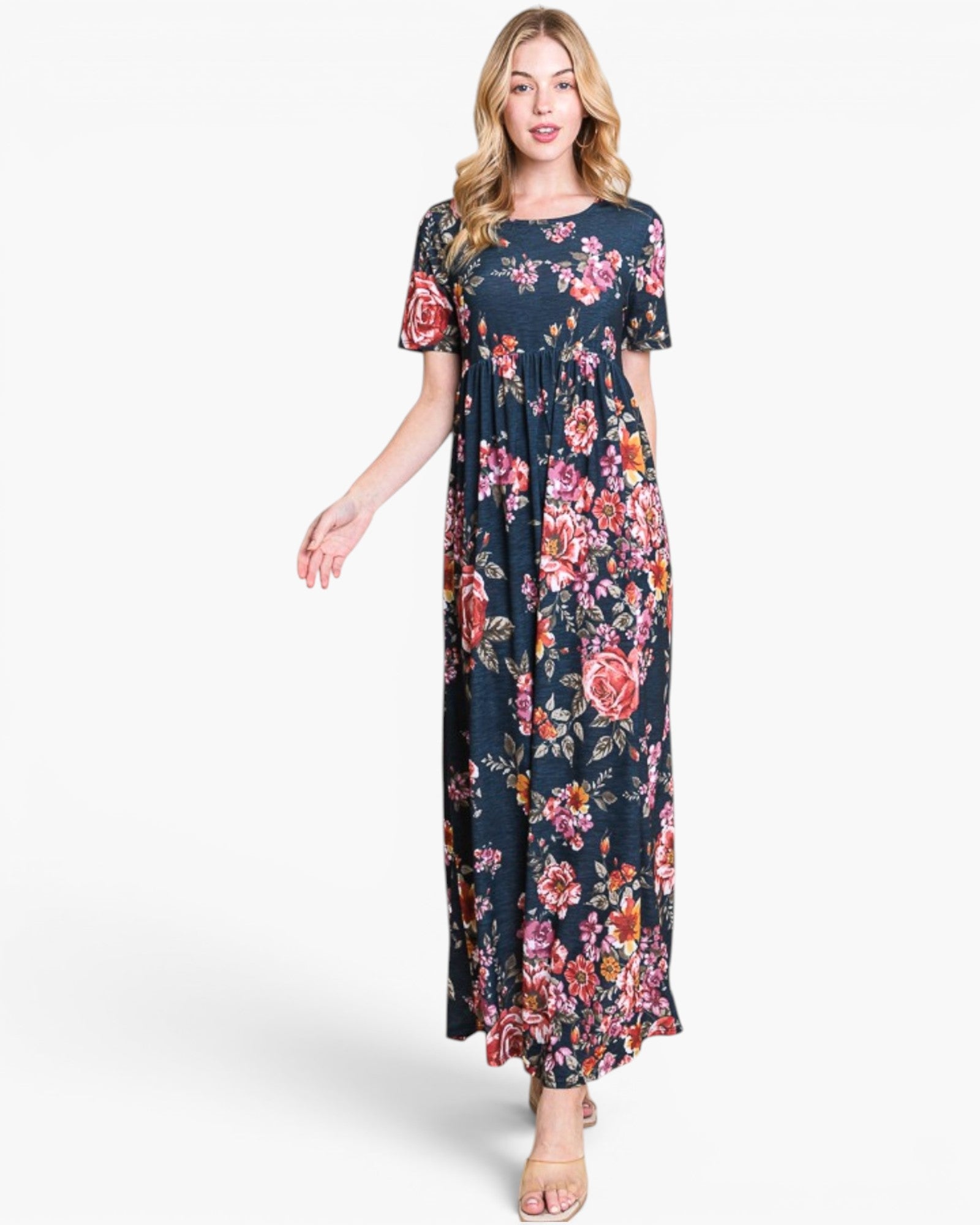 A woman modeling a navy blue maxi dress with a vibrant pink, red, and orange floral print, set against a plain light gray background.