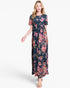 A woman modeling a navy blue maxi dress with a vibrant pink, red, and orange floral print, set against a plain light gray background.