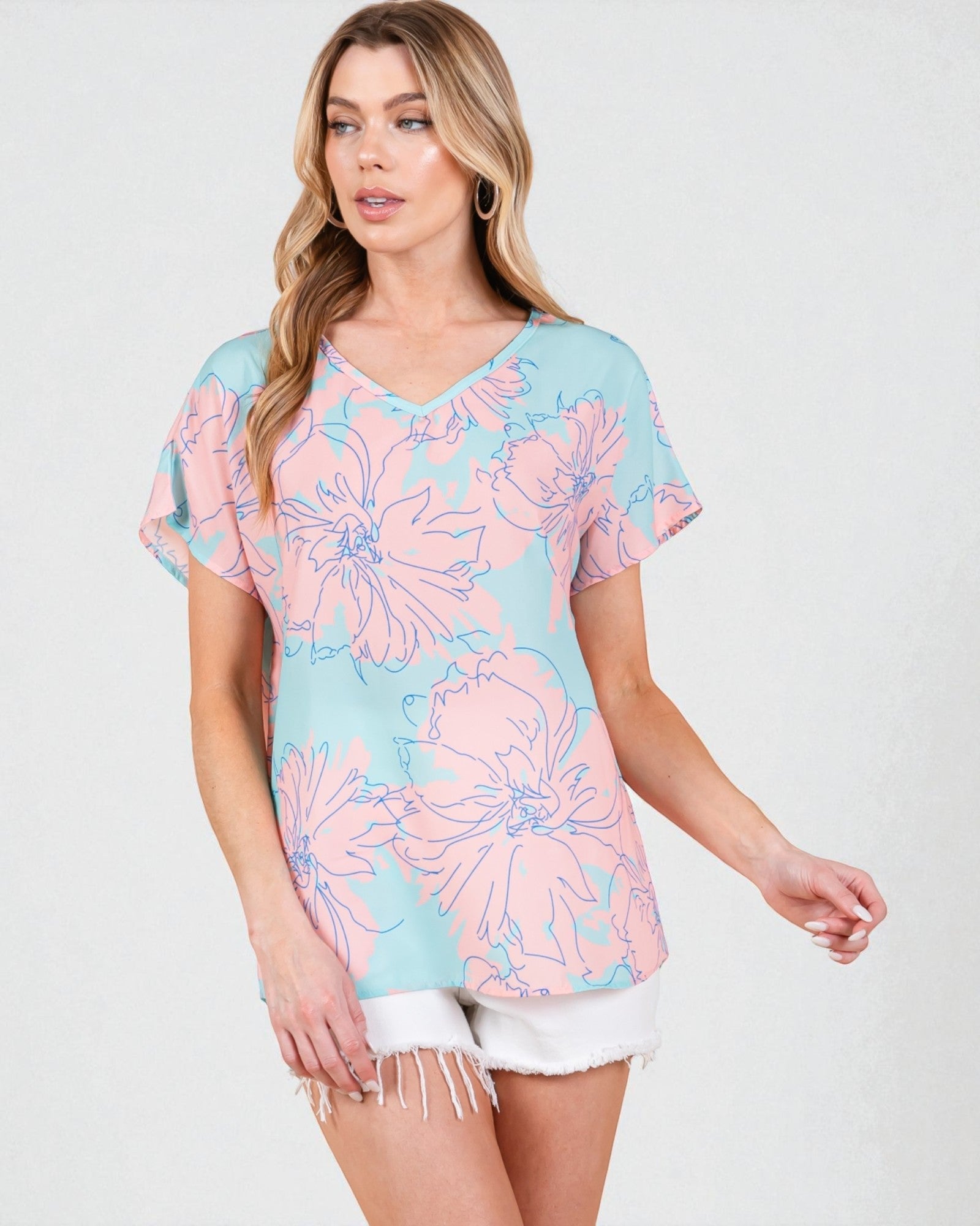 Woman wearing a pastel floral top with white shorts on a light gray background