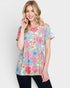 A woman wearing a short-sleeve crewneck t-shirt with a colorful floral print in pink, blue, yellow, and green, paired with black pants, against a light gray background.