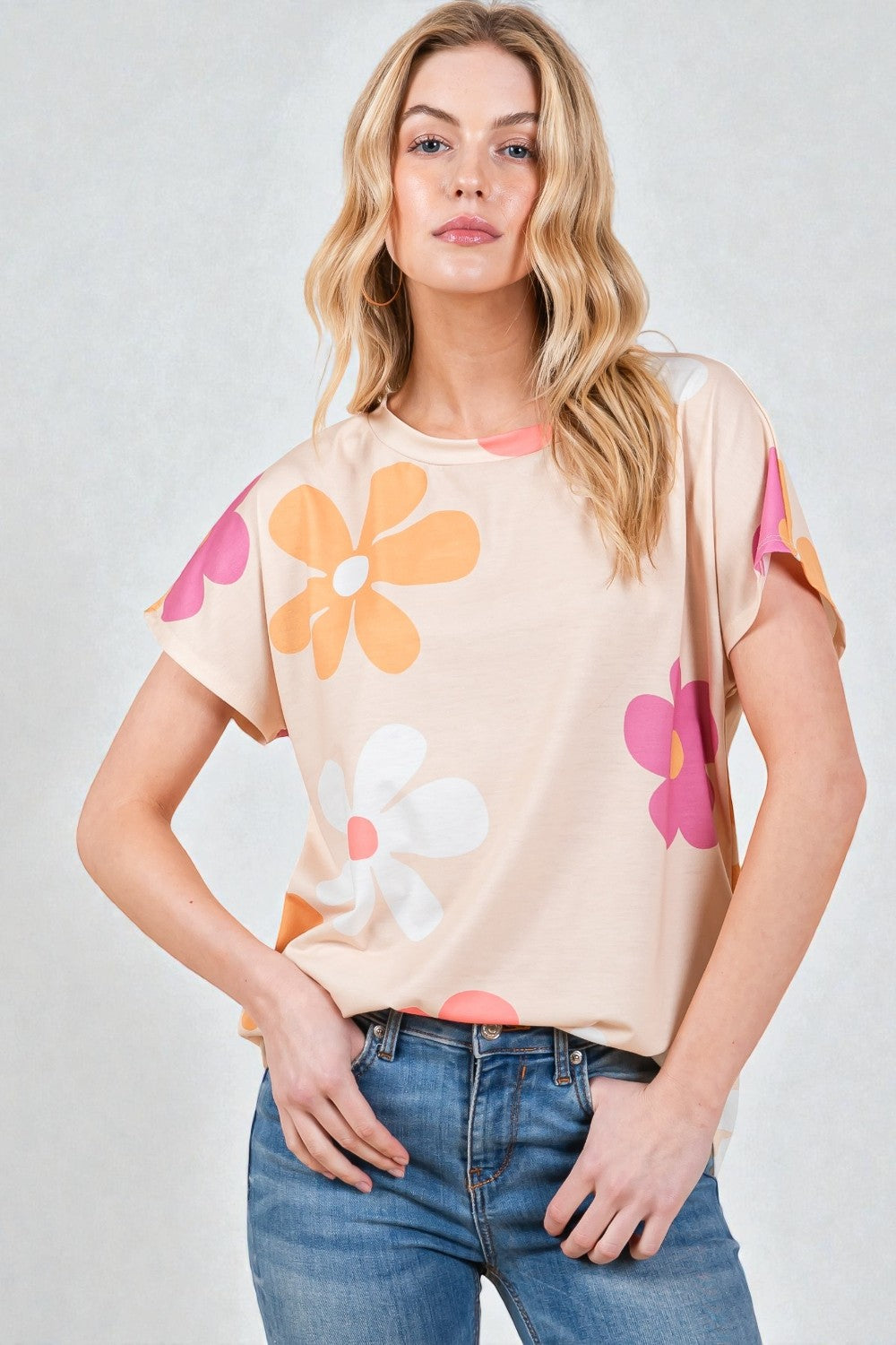 Woman wearing a beige t-shirt with colorful flower designs on a plain background