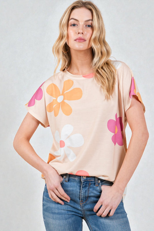 Woman wearing a beige t-shirt with colorful flower designs on a plain background