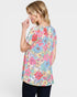 A woman wearing a short-sleeve tunic top with a colorful floral print, shown from a three-quarters back view against a light gray background.