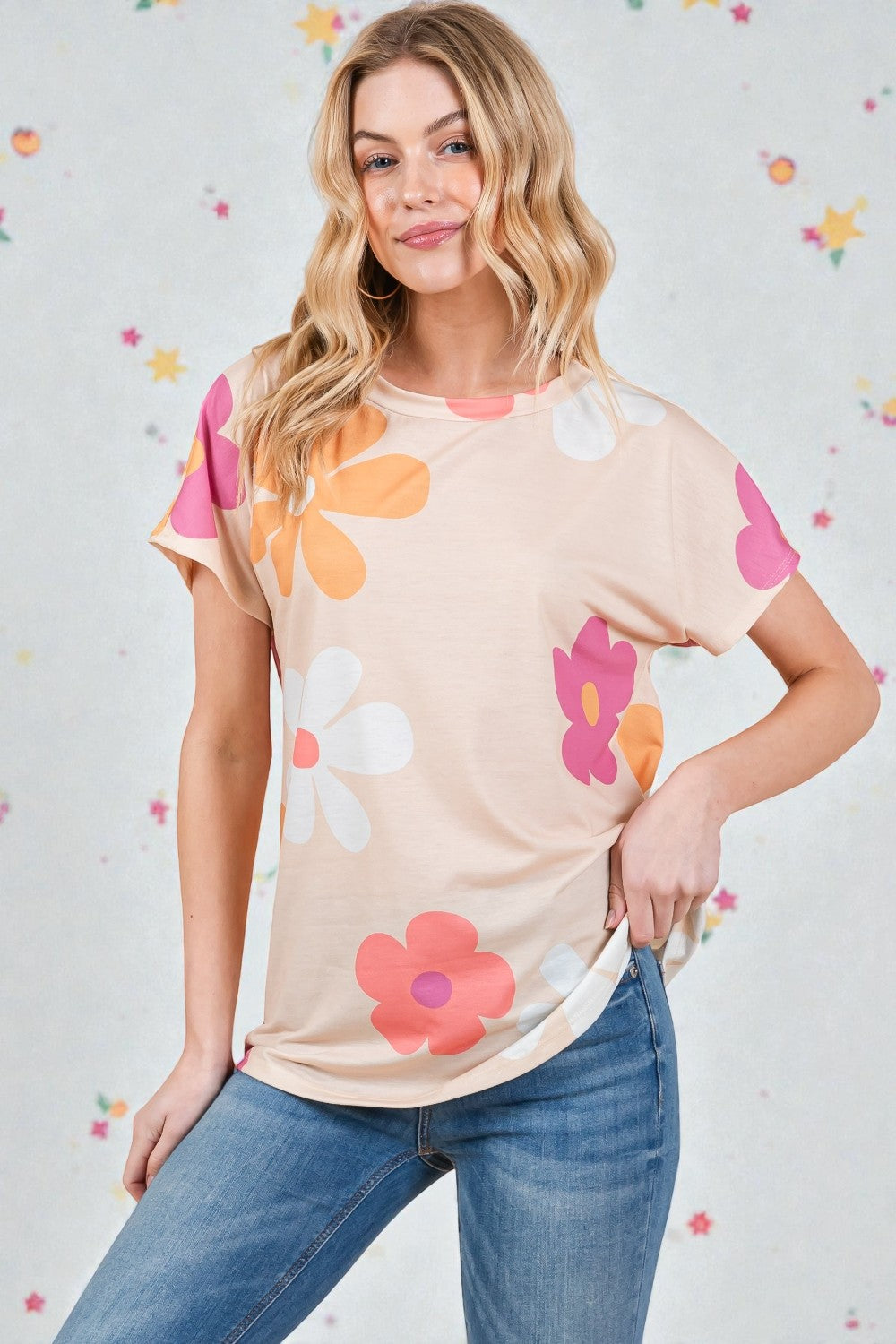 Woman wearing a beige t-shirt with colorful flower patterns against a light gray background with floral decorations.