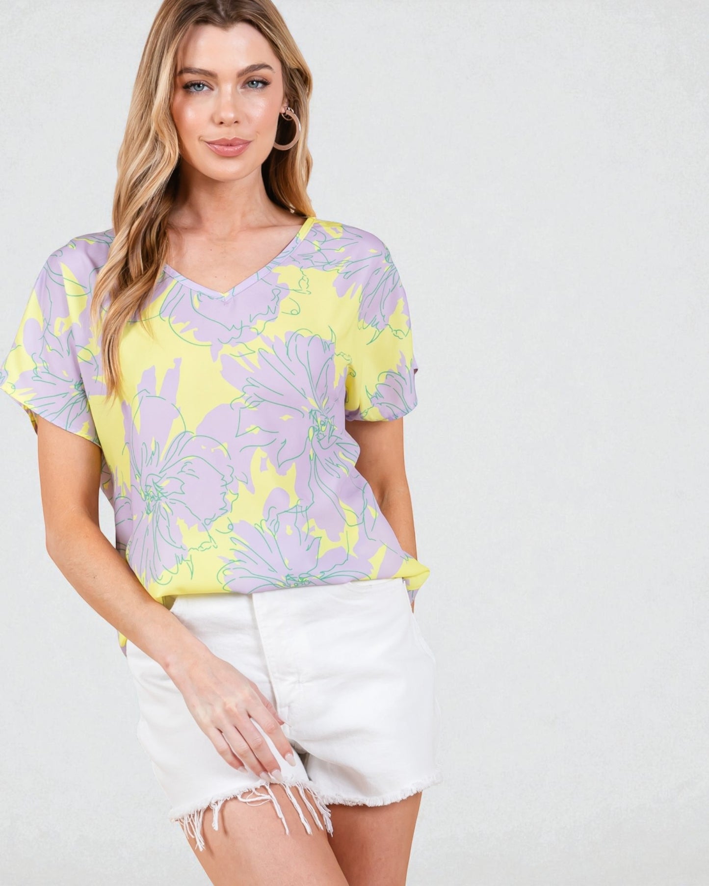 Woman wearing a colorful floral top and white shorts on a plain background