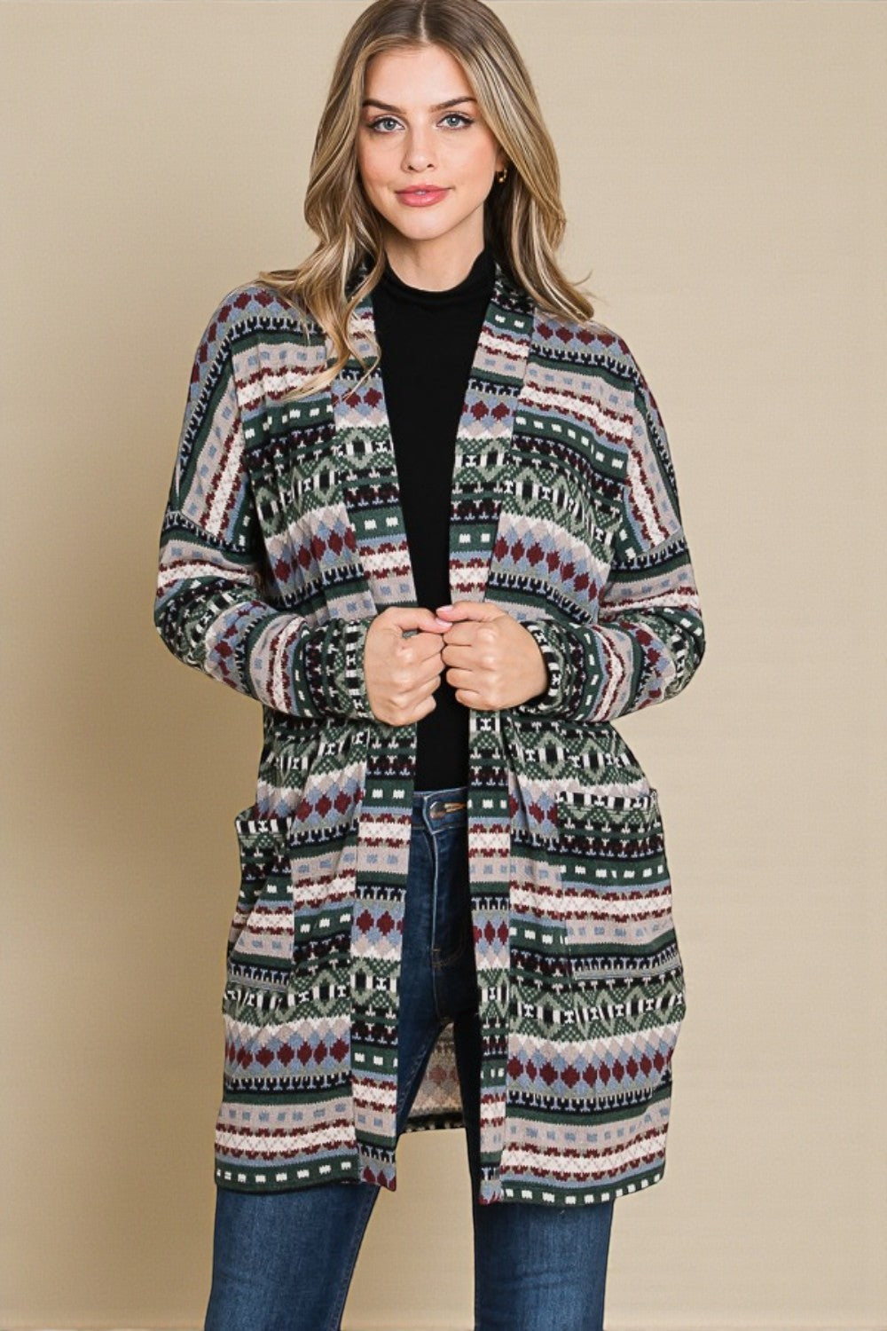 Woman wearing a patterned cardigan over a black top and jeans on a beige background