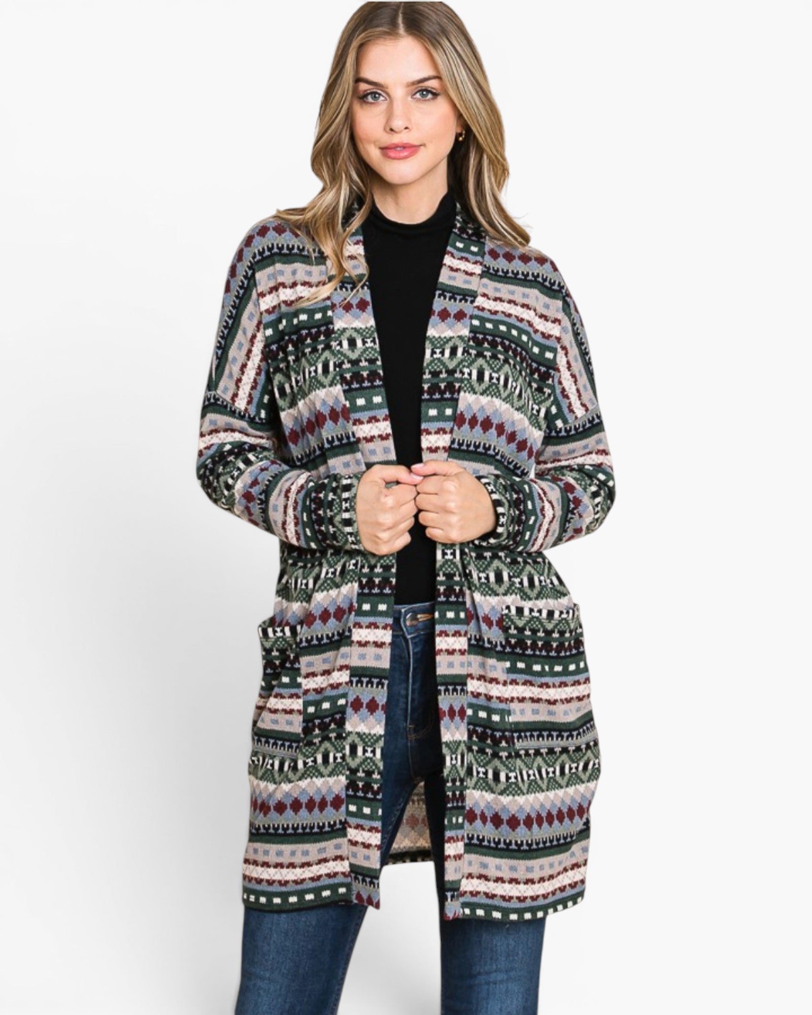A woman modeling a long open-front cardigan with a multicolor geometric Fair Isle pattern in black, green, pink, and white, worn over a black top and blue jeans against a plain white studio background.