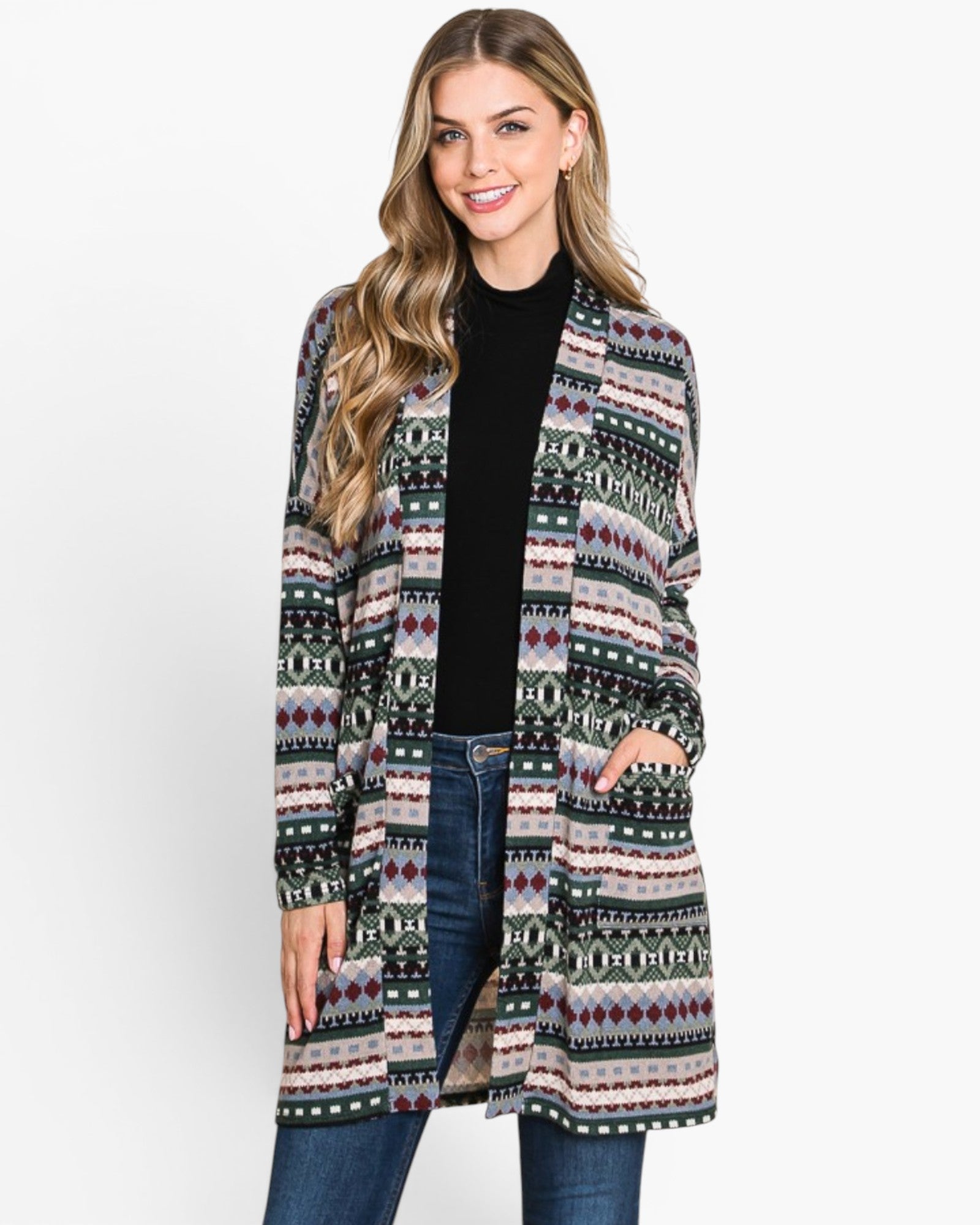 A woman modeling a long open-front cardigan with a multicolor geometric Fair Isle pattern, worn over a black top and blue jeans against a plain white background.