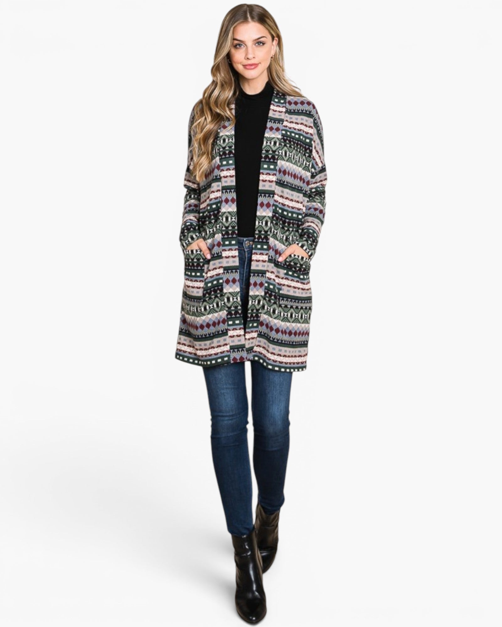 A woman modeling a long open-front cardigan with a multicolor geometric pattern in pink, green, black, and white, worn over a black top and blue jeans against a light gray studio background.