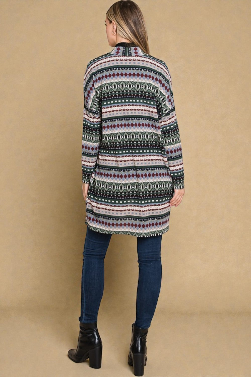 Person wearing a patterned cardigan and blue jeans against a beige background