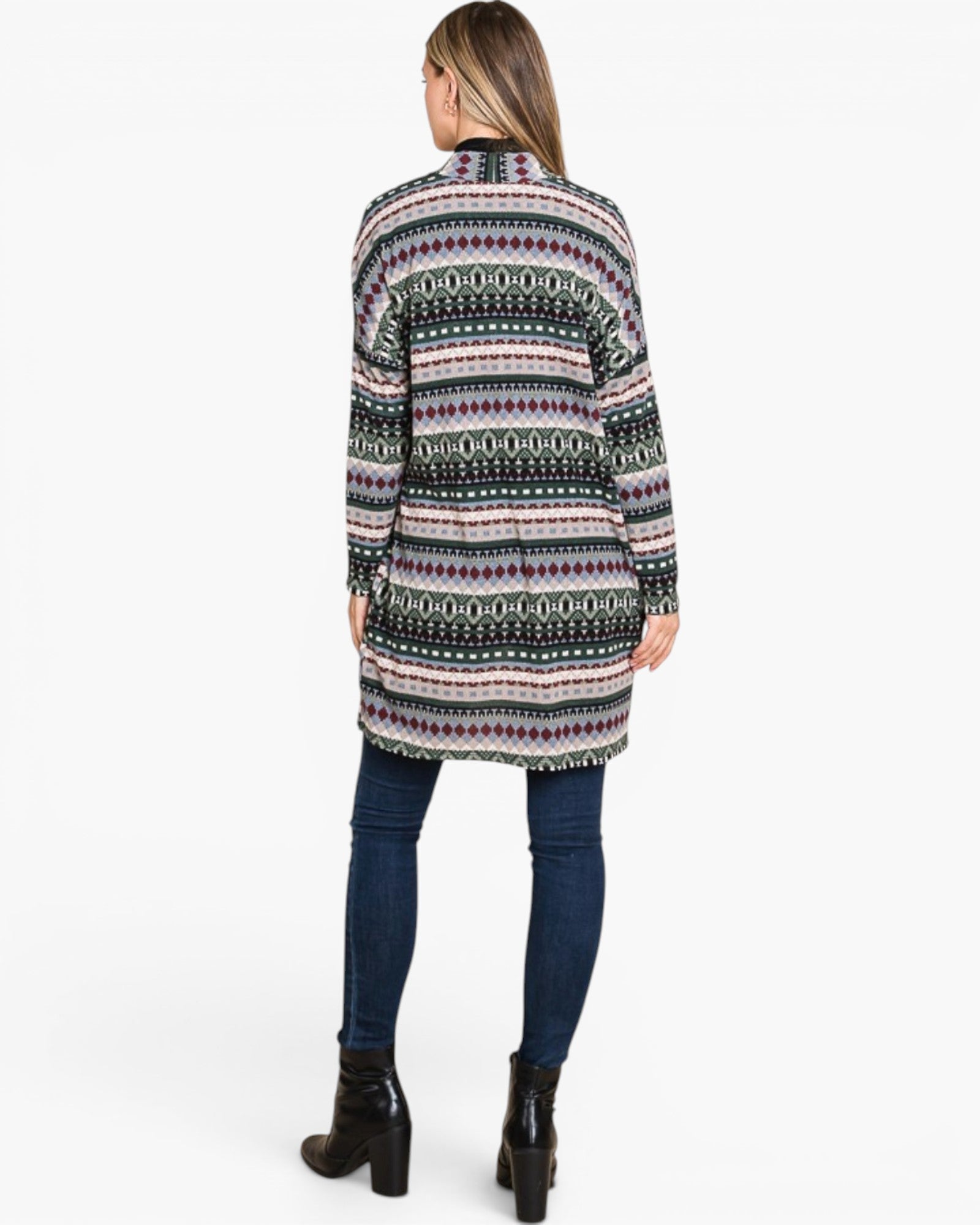 A woman viewed from the back wearing a long-sleeve knit cardigan with a multicolor geometric pattern, paired with dark blue skinny jeans and black ankle boots, against a plain white studio background.