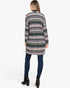 A woman viewed from the back wearing a long-sleeve knit cardigan with a multicolor geometric pattern, paired with dark blue skinny jeans and black ankle boots, against a plain white studio background.