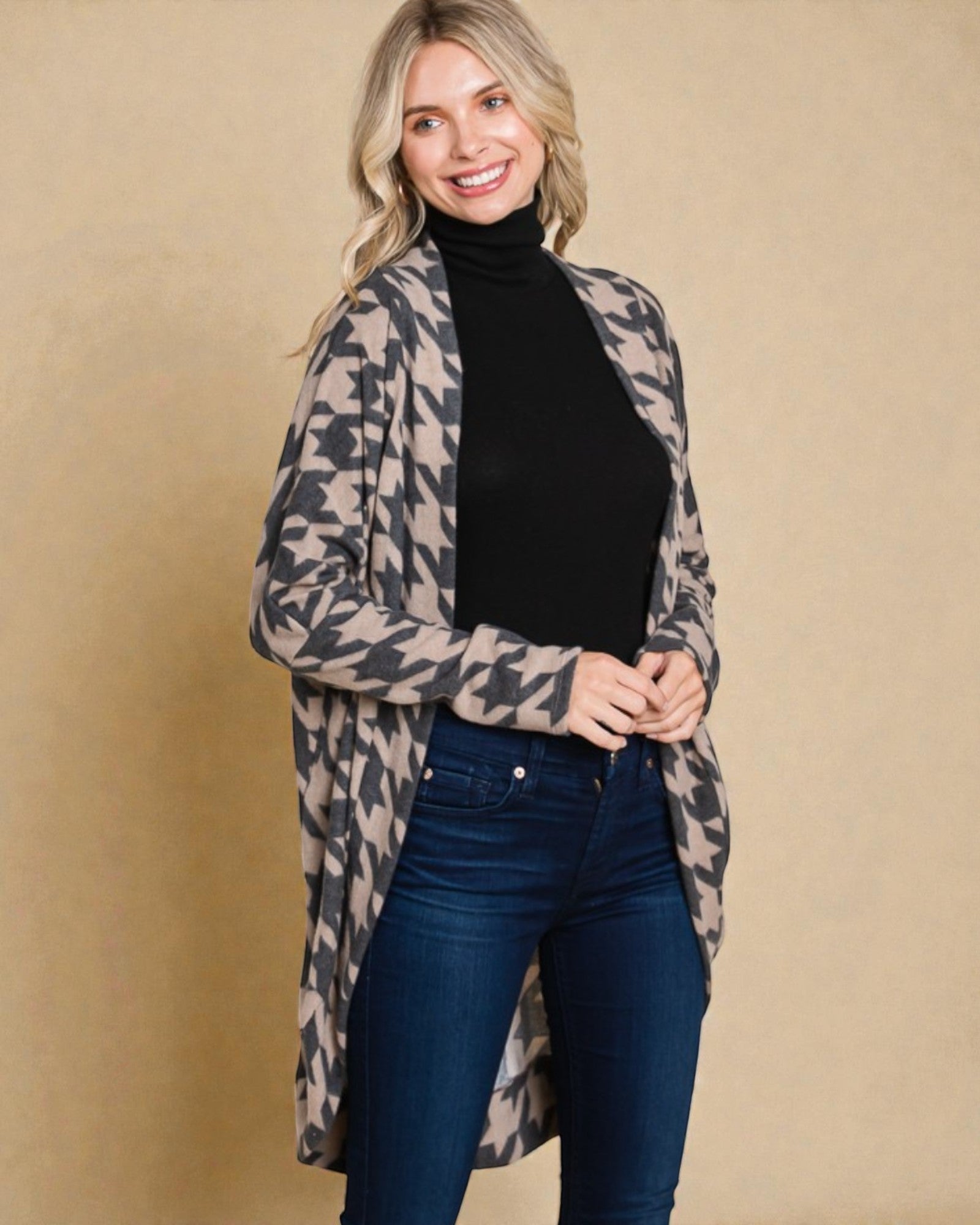 Woman wearing a patterned cardigan over a black turtleneck and blue jeans on a beige background