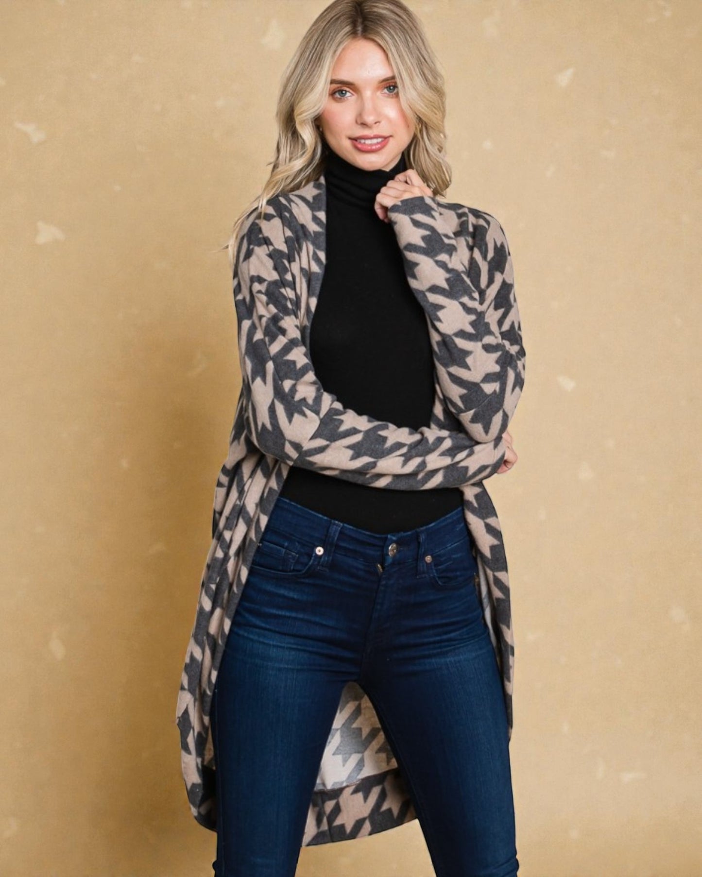 Woman wearing a patterned cardigan over a black turtleneck and blue jeans against a beige background