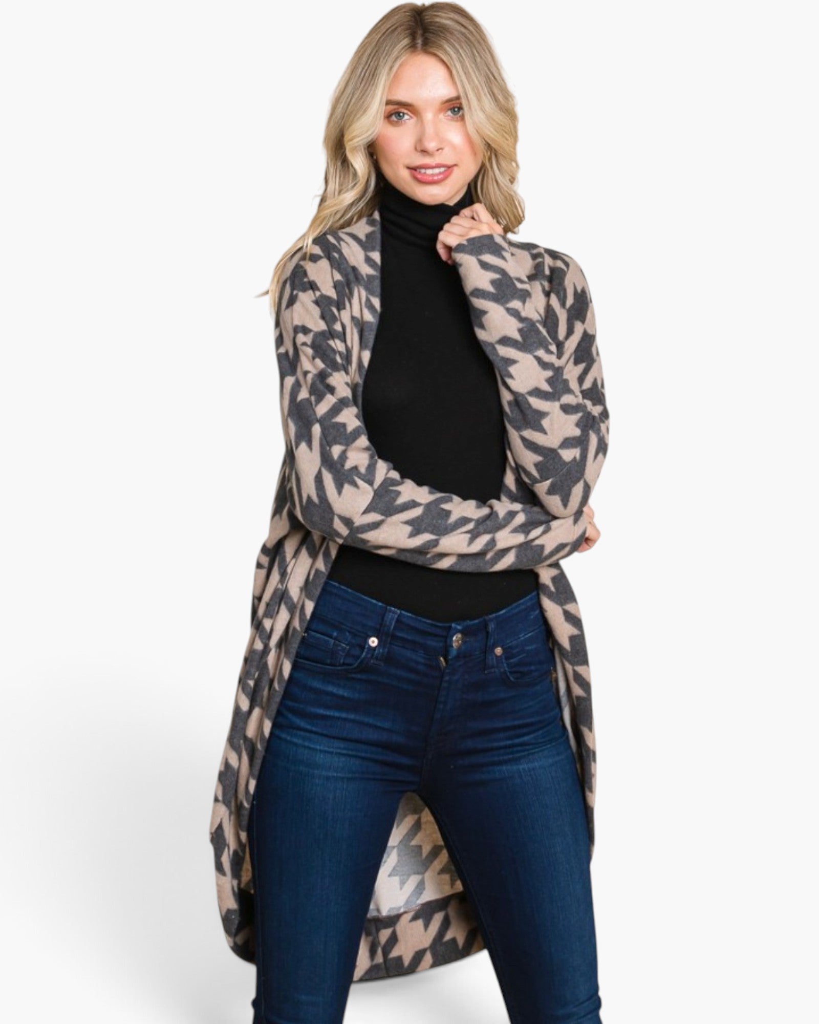A woman modeling a beige and gray houndstooth patterned open-front cardigan over a black turtleneck and dark blue jeans, photographed against a clean white studio background.