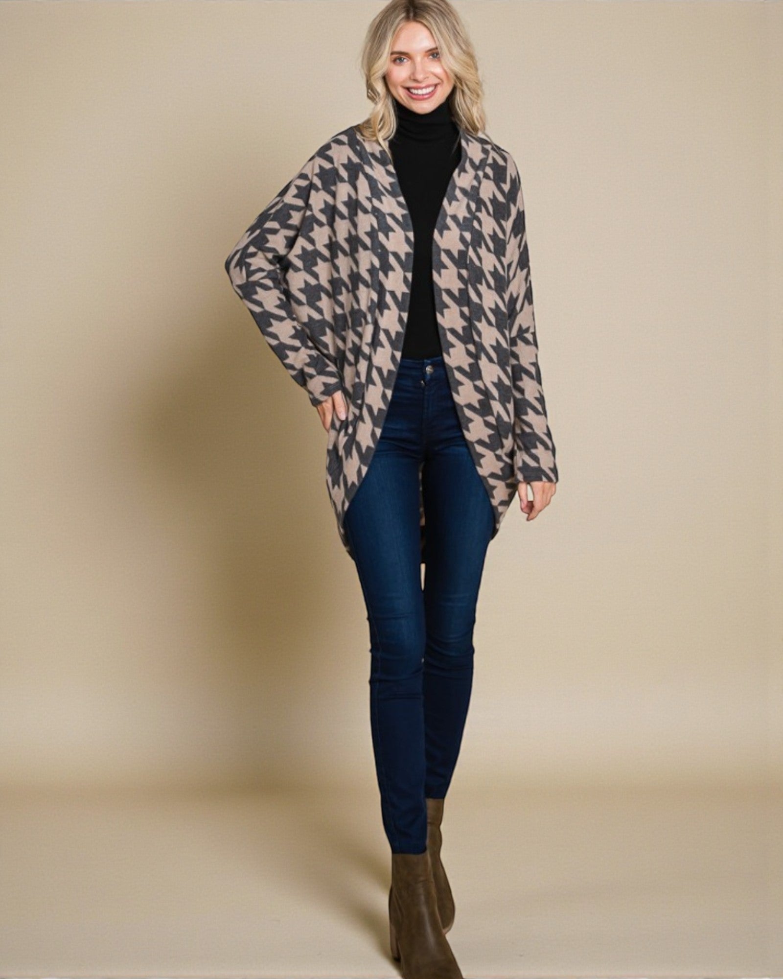 Woman wearing a patterned coat over a black top and blue jeans on a beige background
