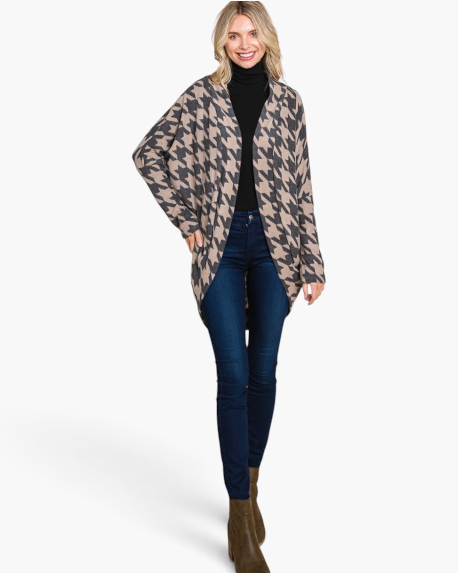 A woman modeling a beige and dark gray houndstooth patterned open-front cardigan over a black turtleneck, paired with dark blue skinny jeans and brown ankle boots, against a plain white studio background.