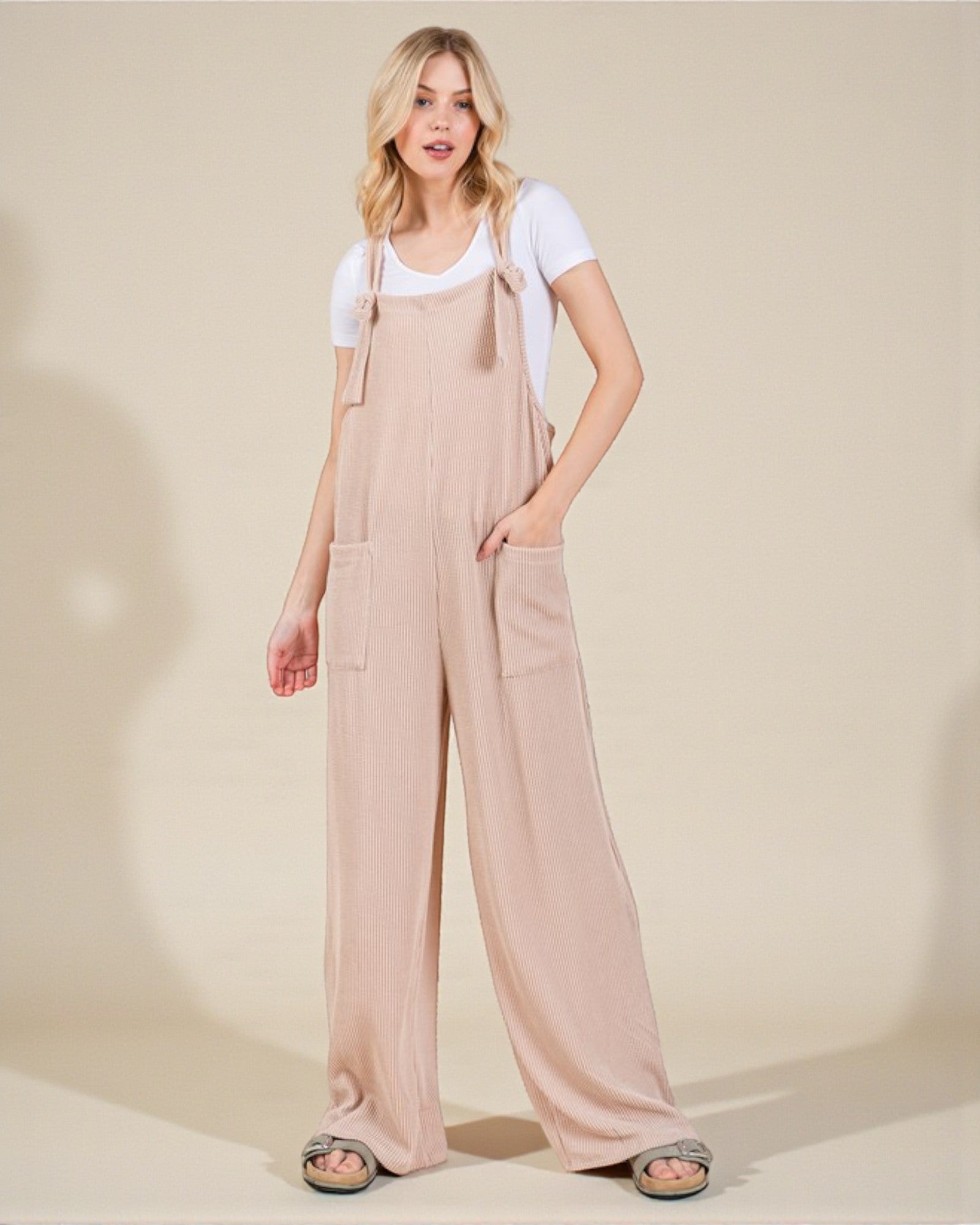 Woman wearing beige overalls and a white t-shirt on a plain background