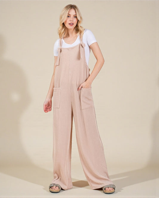 Woman wearing beige overalls and a white t-shirt on a plain background