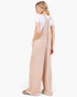 A woman shown from the back wearing a light beige wide-leg overall jumpsuit over a white short-sleeve t-shirt, photographed against a clean white studio background.