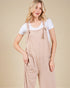 Woman wearing beige overalls with a plain background