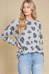 Woman wearing a gray sweater with a leopard print pattern and blue jeans against a beige background