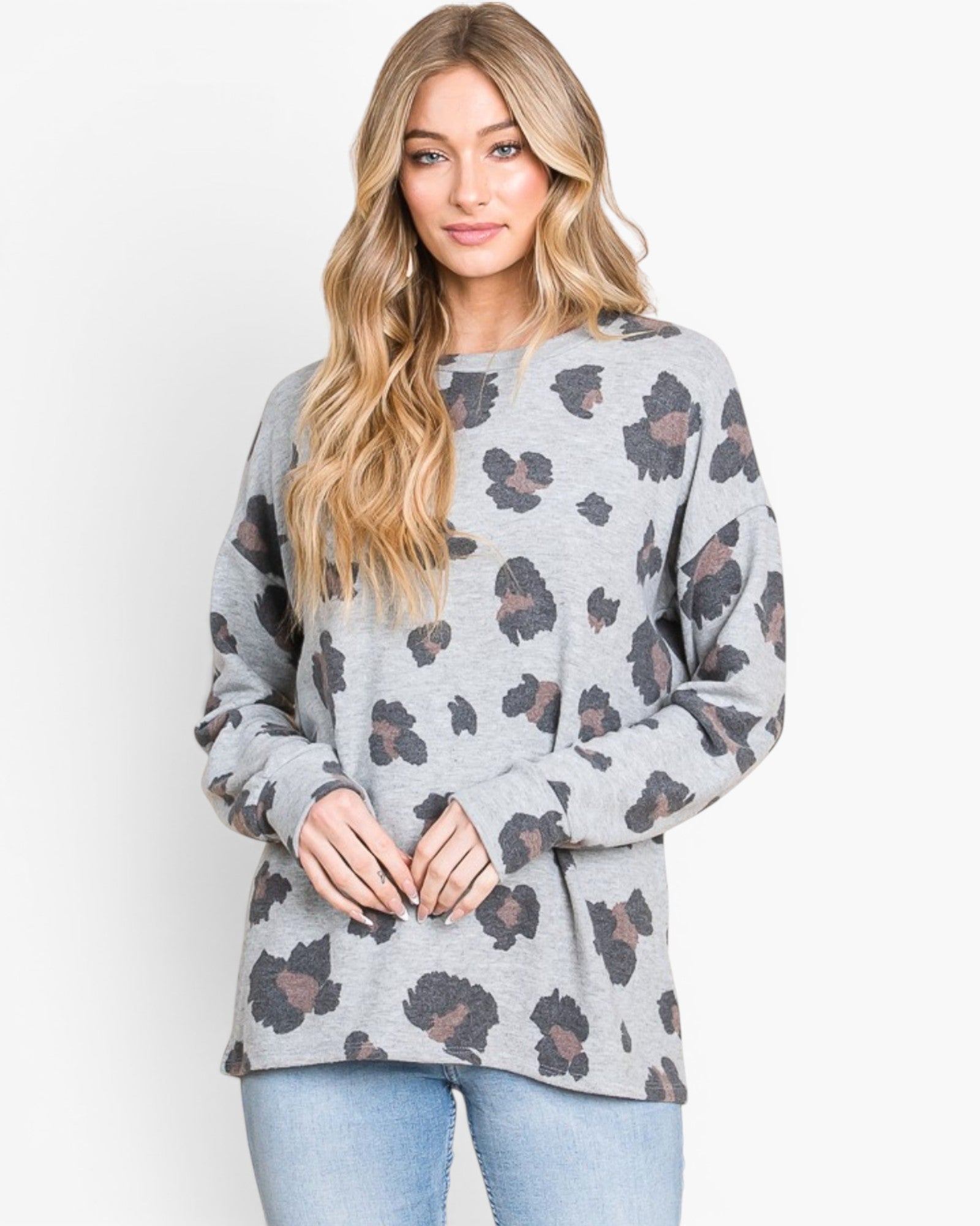 A woman wearing a light gray long-sleeve crewneck sweatshirt with a dark gray and brown leopard print pattern, paired with light blue jeans, against a plain white background.