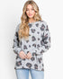 A woman wearing a light gray long-sleeve crewneck sweatshirt with a dark gray and brown leopard print pattern, paired with light blue jeans, against a plain white background.