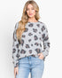 A woman modeling a light gray crewneck sweatshirt with a dark brown and charcoal leopard print, paired with light blue jeans, against a plain white studio background.
