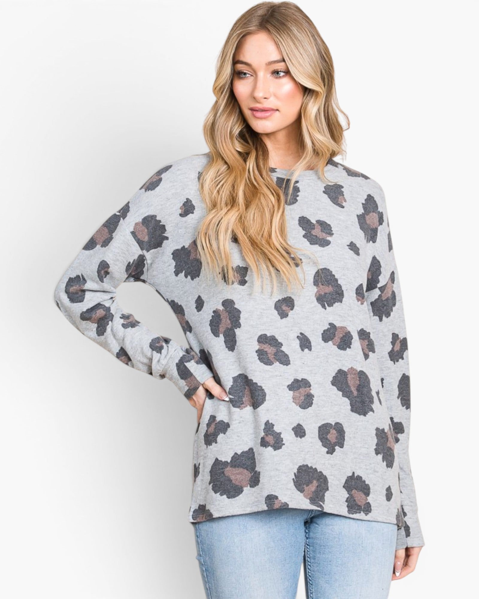 A woman modeling a light gray long-sleeve top with a dark gray and brown leopard print pattern, paired with light blue jeans, against a plain white studio background.
