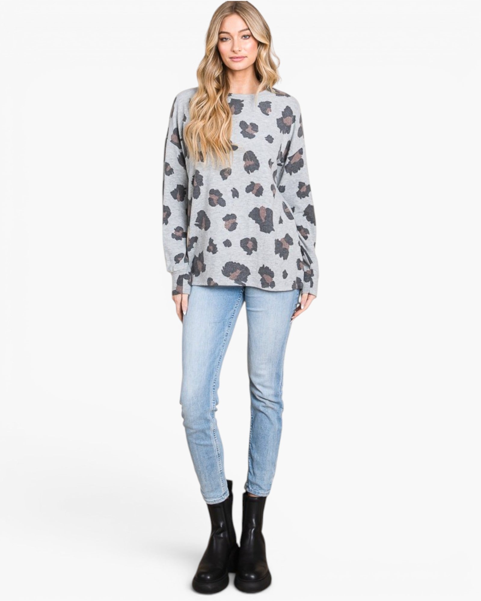 A woman modeling a light gray long-sleeve sweatshirt with a dark gray and black leopard print, paired with light blue skinny jeans and black ankle boots, against a plain white studio background.