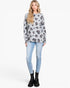 A woman modeling a light gray long-sleeve sweatshirt with a dark gray and black leopard print, paired with light blue skinny jeans and black ankle boots, against a plain white studio background.
