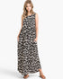 A woman modeling a sleeveless, one-shoulder maxi dress with a black and off-white leopard print pattern, standing against a light gray studio background.