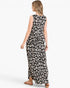 A woman modeling a sleeveless black maxi dress with a white abstract animal print pattern, shown from a rear three-quarter view against a plain white studio background.