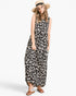 A woman modeling a sleeveless black and white leopard print maxi dress, styled with a straw hat and brown leather slide sandals, against a plain white studio background.