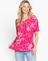 A woman modeling a short-sleeve pink top with a darker pink leopard print pattern, paired with light blue jeans, against a plain white background.