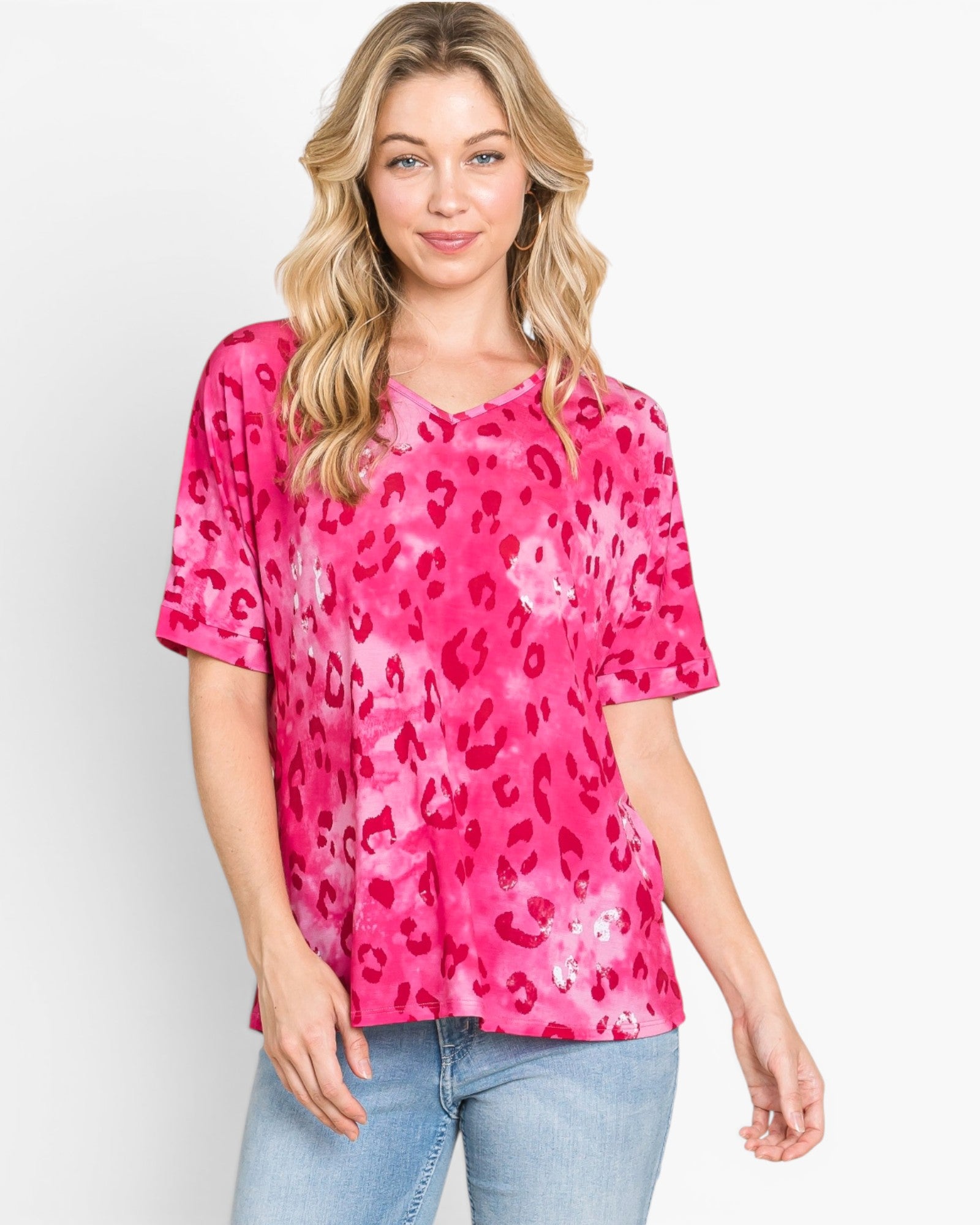A woman modeling a short-sleeve pink top with a darker pink leopard print pattern, paired with light blue jeans, against a plain white background.