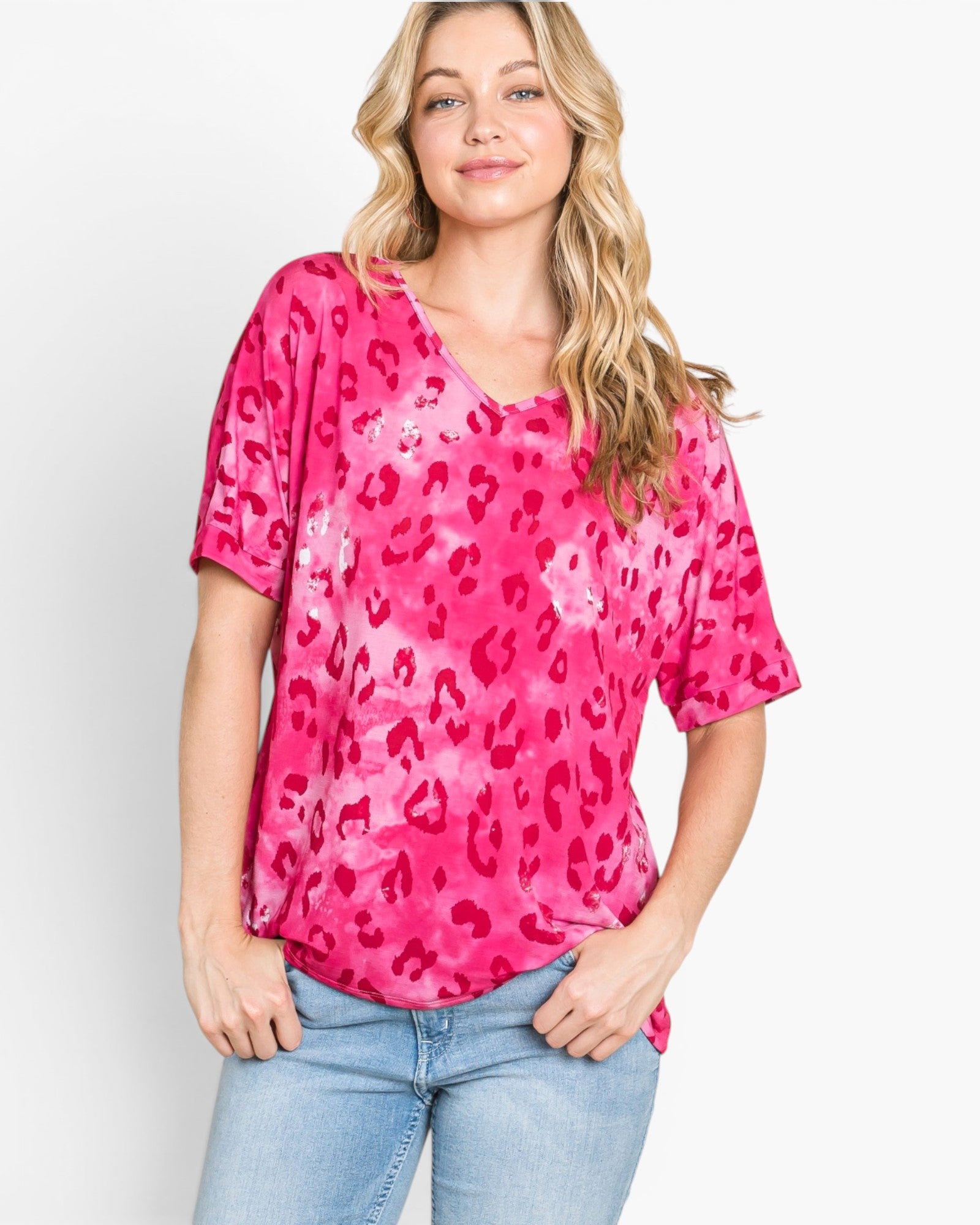 A woman wearing a bright pink short-sleeve V-neck top with a darker pink leopard print pattern, paired with light blue jeans, against a plain white background.
