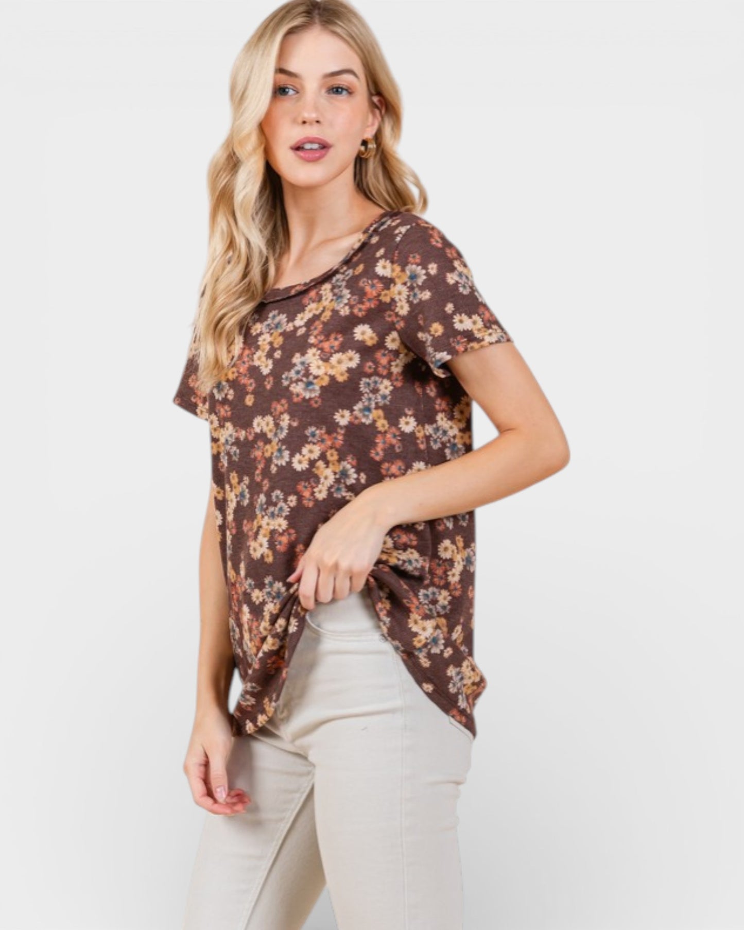 Woman wearing a brown floral top and white pants on a light background