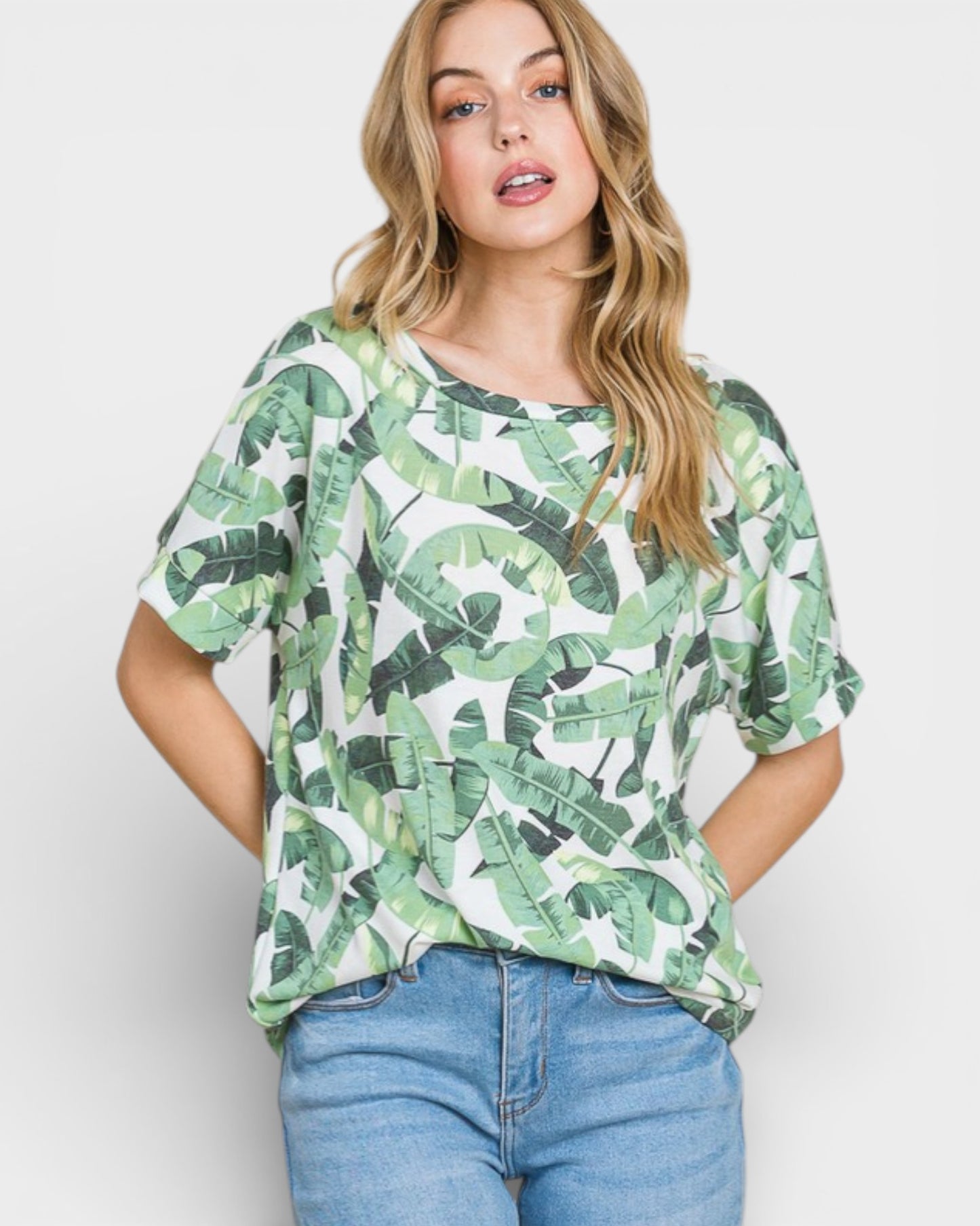 Woman wearing a green leaf-patterned top and blue jeans on a white background