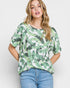 Woman wearing a green leaf-patterned top and blue jeans on a white background