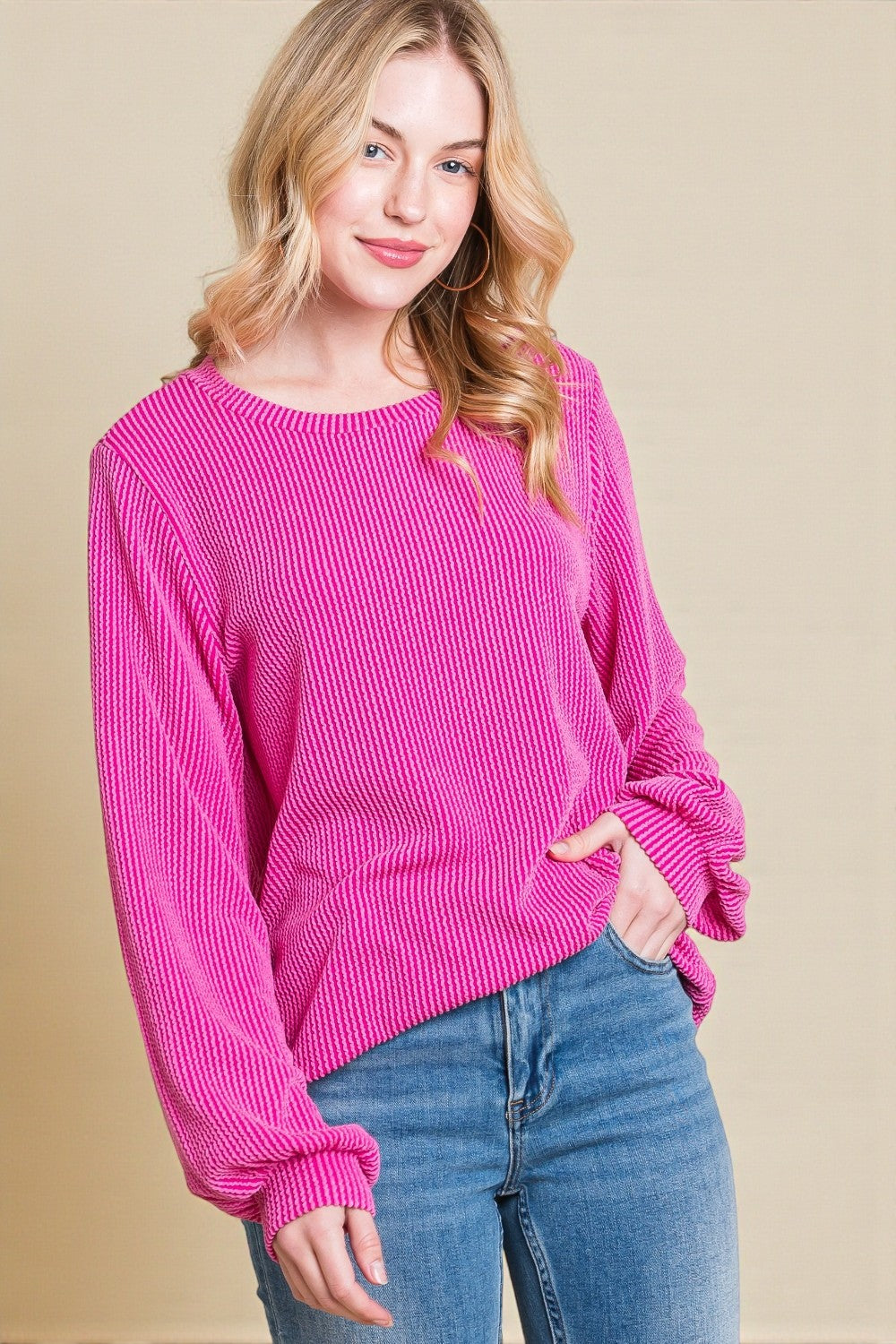 Woman wearing a bright pink sweater and blue jeans on a beige background