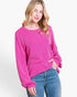 A woman wearing a bright pink ribbed knit long-sleeve top with blue jeans, photographed against a clean white studio background.