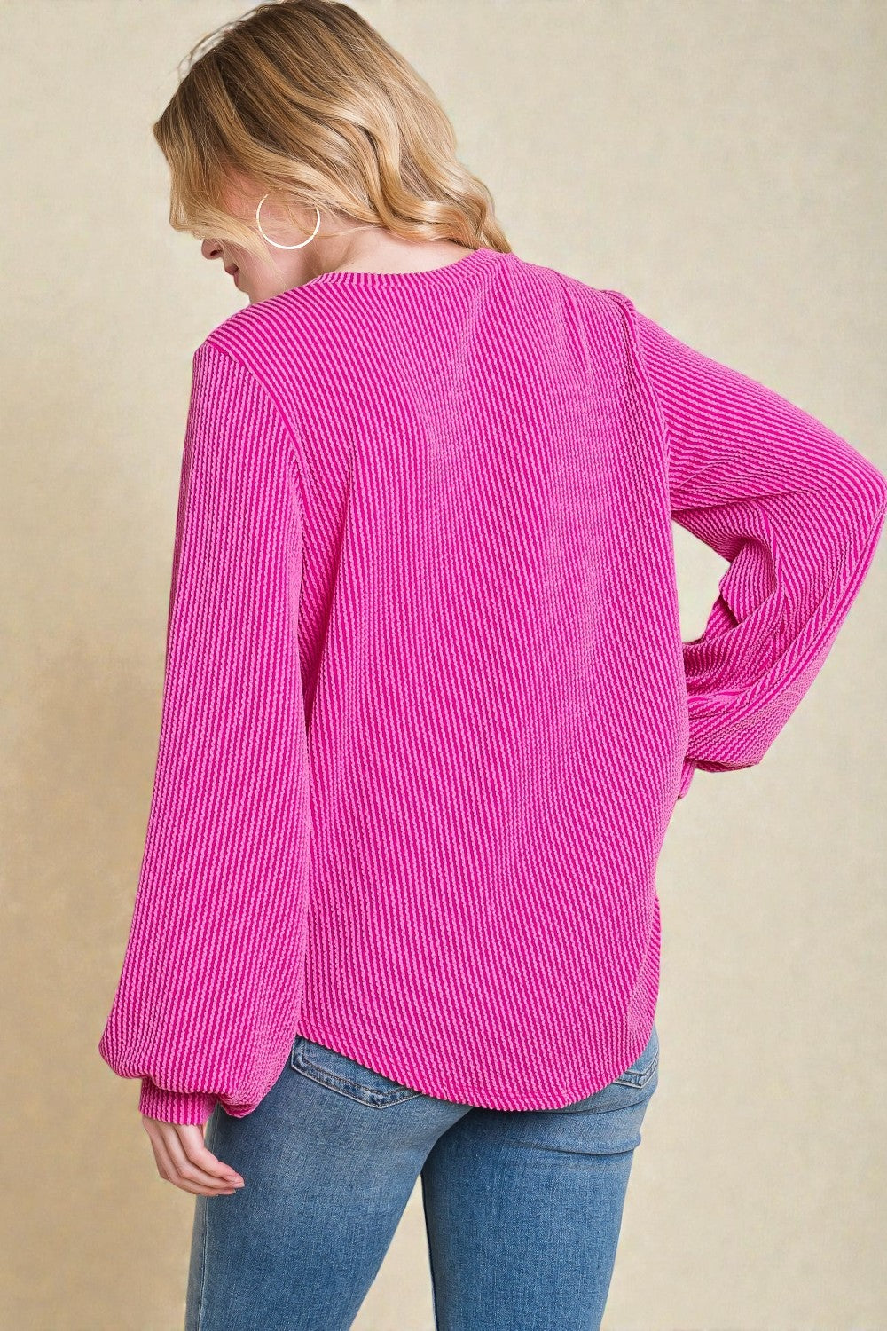 Person wearing a bright pink ribbed sweater and blue jeans on a beige background