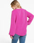 A woman wearing a bright pink long-sleeve top with vertical textured stripes, shown from a back-three-quarter angle against a plain white background.