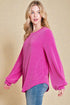 Woman wearing a bright pink sweater and blue jeans against a beige background